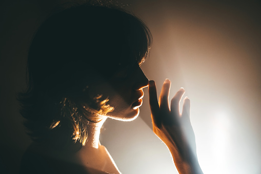 A woman is seen in silhouette, holding her hand to her face.
